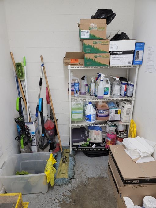 Garage storage area with shelves of paint cans and supplies, brooms, boxes, and a trash bin