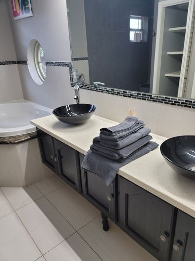 Bathroom vanity with two black sinks, folded gray towels, mirror, and tiled countertop