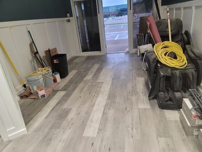 Renovated room with light wood flooring, tools and supplies along the walls, and an open doorway to outside.
