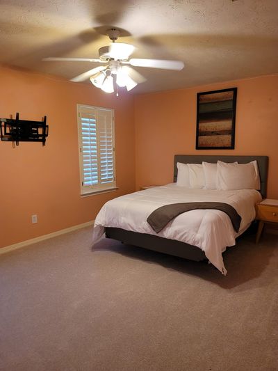 Bedroom with peach walls, white ceiling fan, window blinds, and a bed with white bedding.
