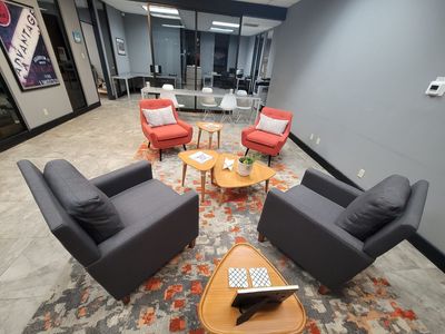 Office lounge with four chairs around low tables on a patterned rug in a modern gray room