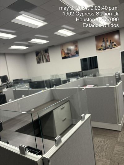 Cubicle office with gray desks and partitions, fluorescent lights, and wall art in a bank branch.