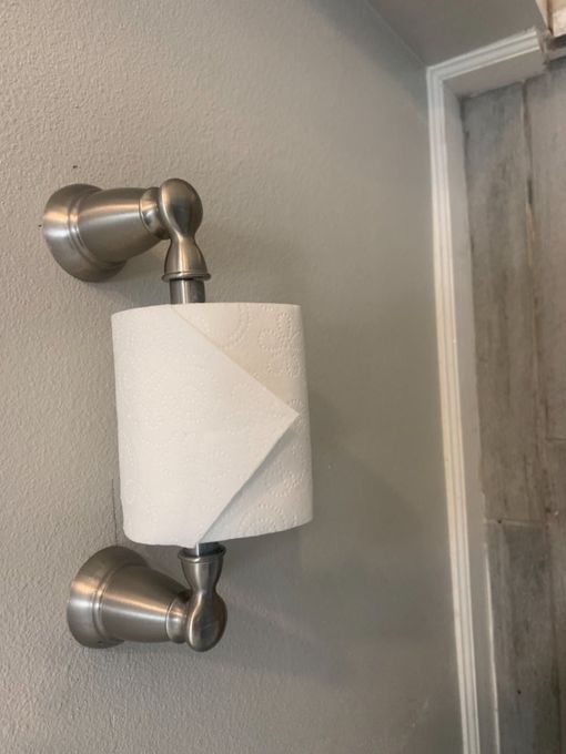 Wall-mounted metal toilet paper holder with a roll of white paper in a bathroom.