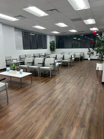 Empty waiting room with gray chairs, wood floors, tables, and bright ceiling lights