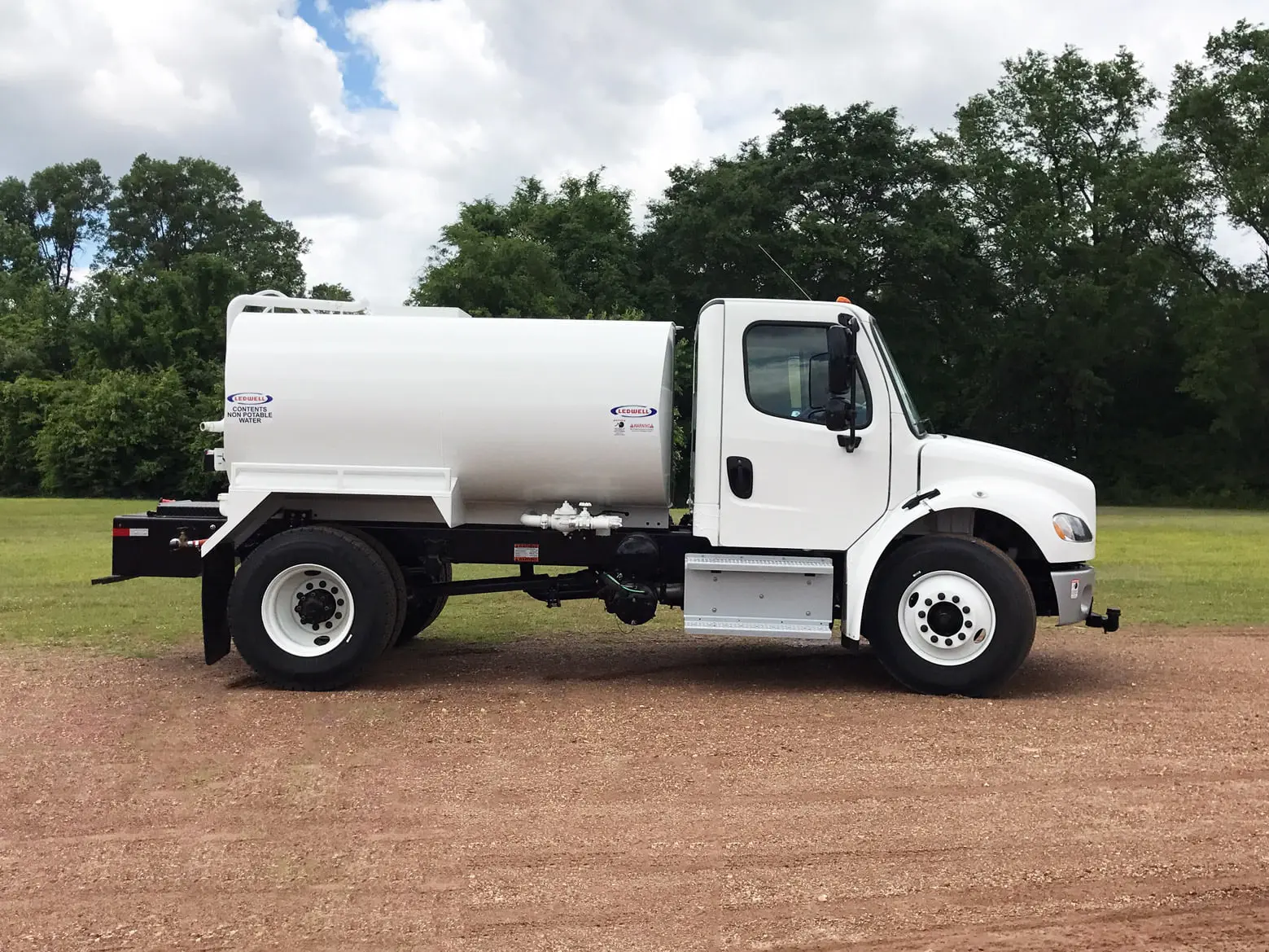 A white tanker truck is parked in a gravel lot