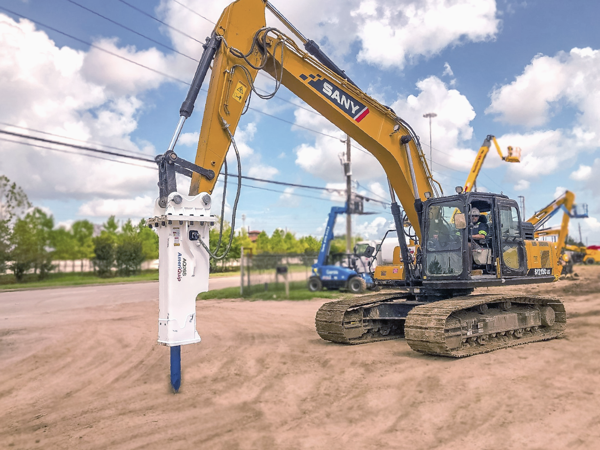 A yellow and black excavator with a hammer attached to it is parked in a dirt lot.