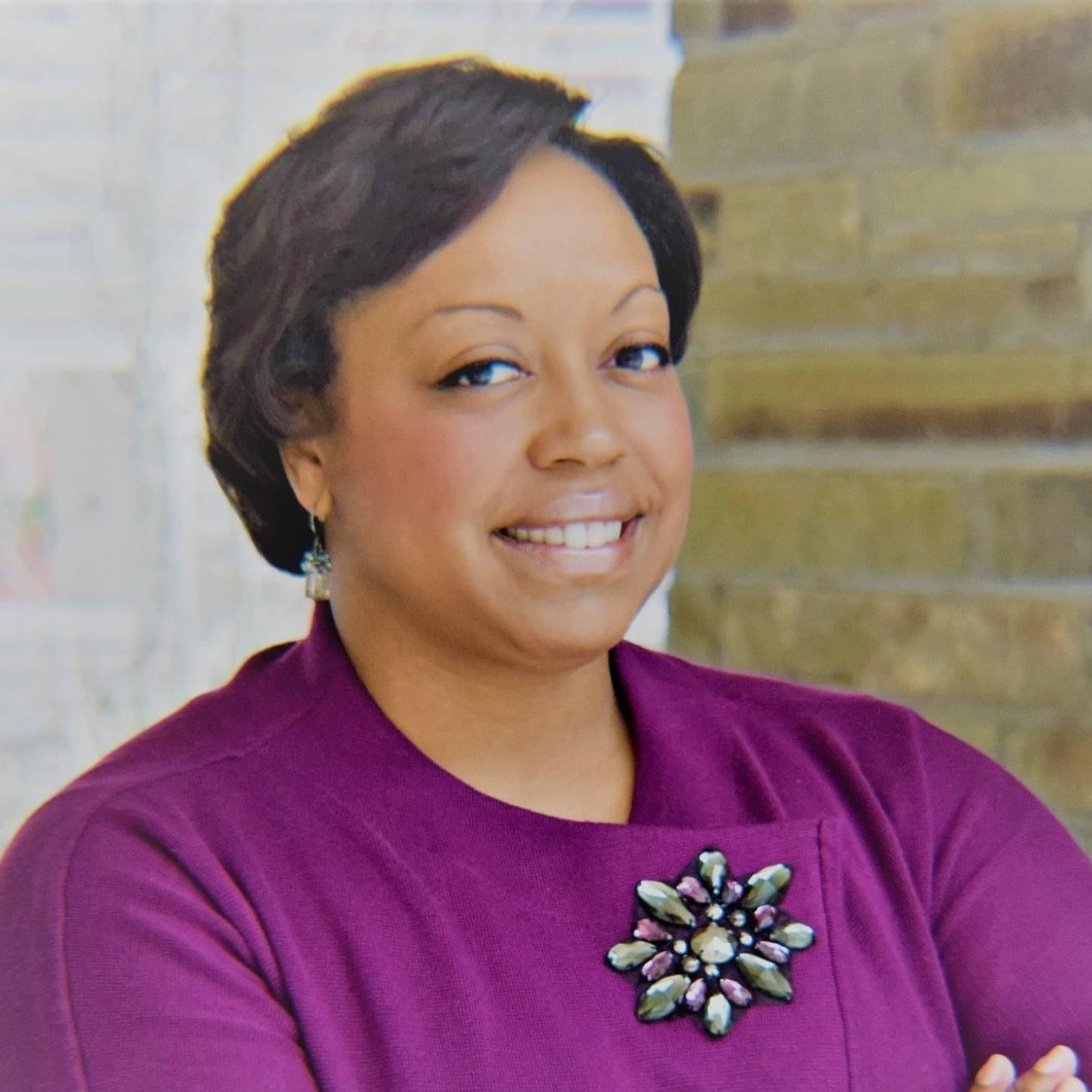 A woman wearing a green jacket and a black shirt is smiling.