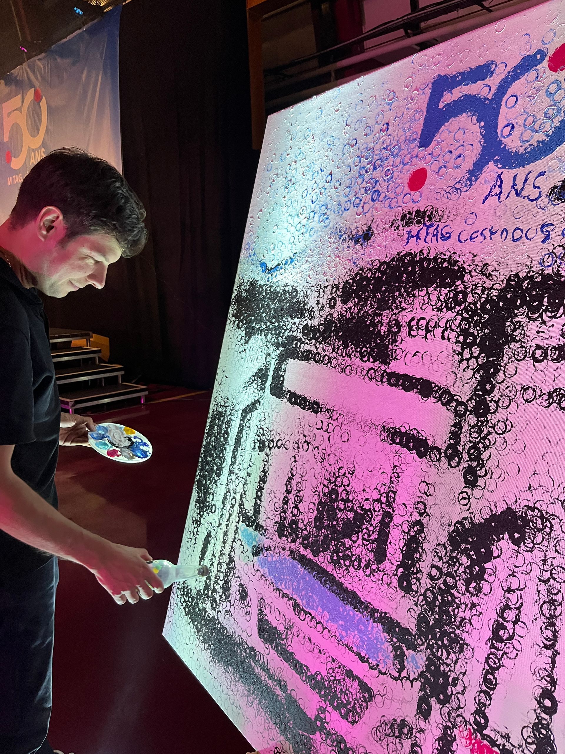 Artiste pulvérisant de la peinture sur une grande toile, révélant partiellement un motif en noir, blanc et rose.