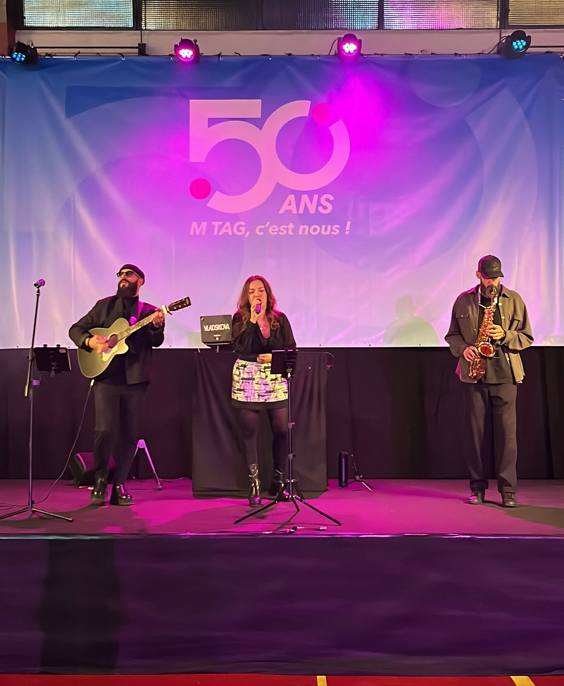 Le groupe se produit sur scène, devant une banderole célébrant un 50e anniversaire.