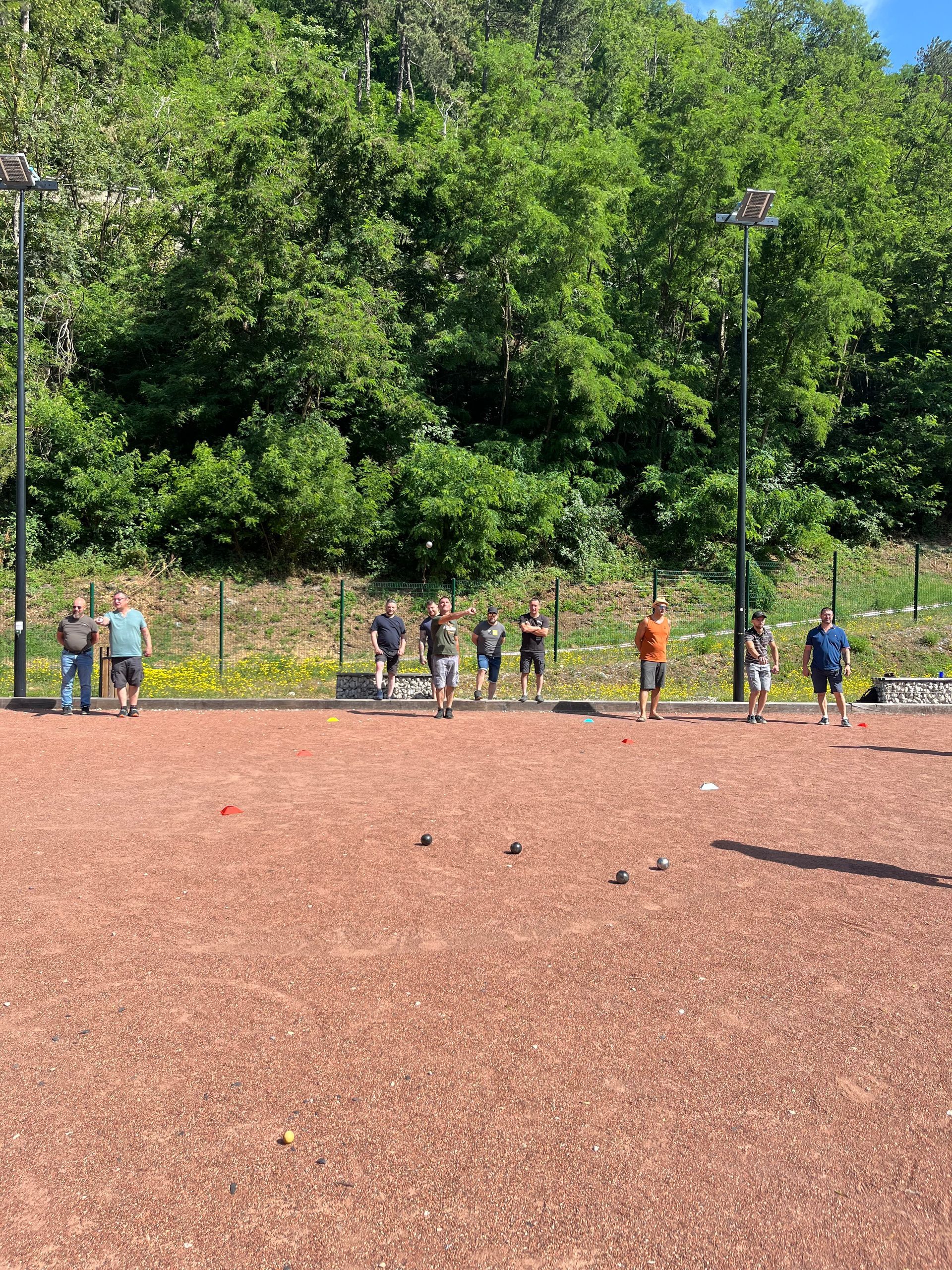 Un groupe de personnes se tient debout sur un champ de terre pour jouer à la pétanque.
