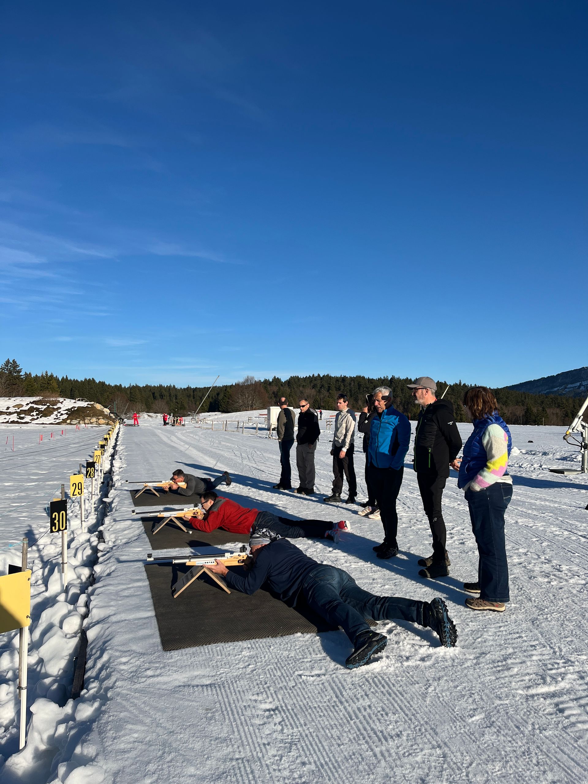 Des personnes s'entraînent au tir sur un stand de tir extérieur enneigé par une journée ensoleillée.
