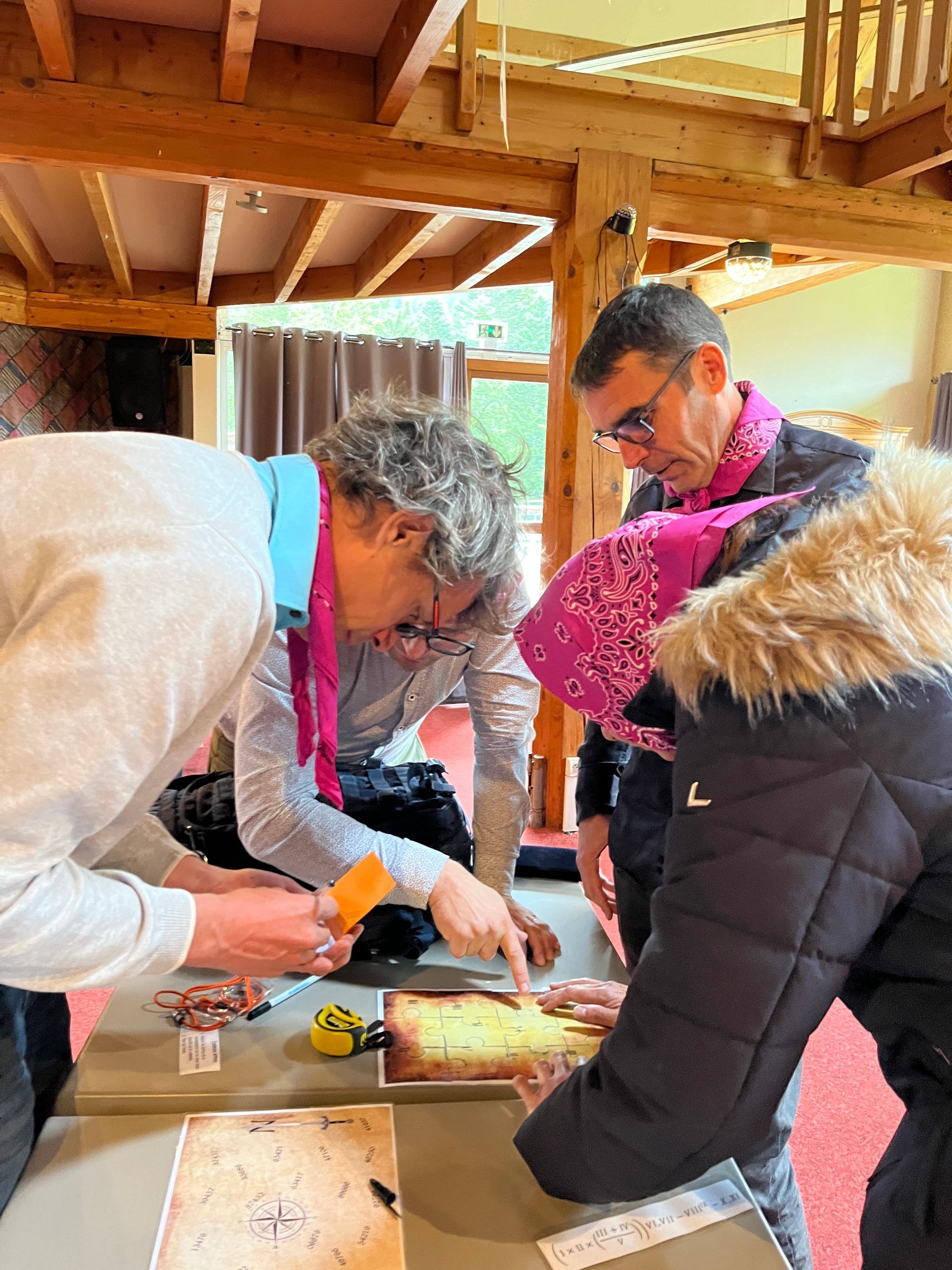 Les gens se sont rassemblés autour d'une table, examinant une carte, utilisant des outils, dans un bâtiment rustique en bois.