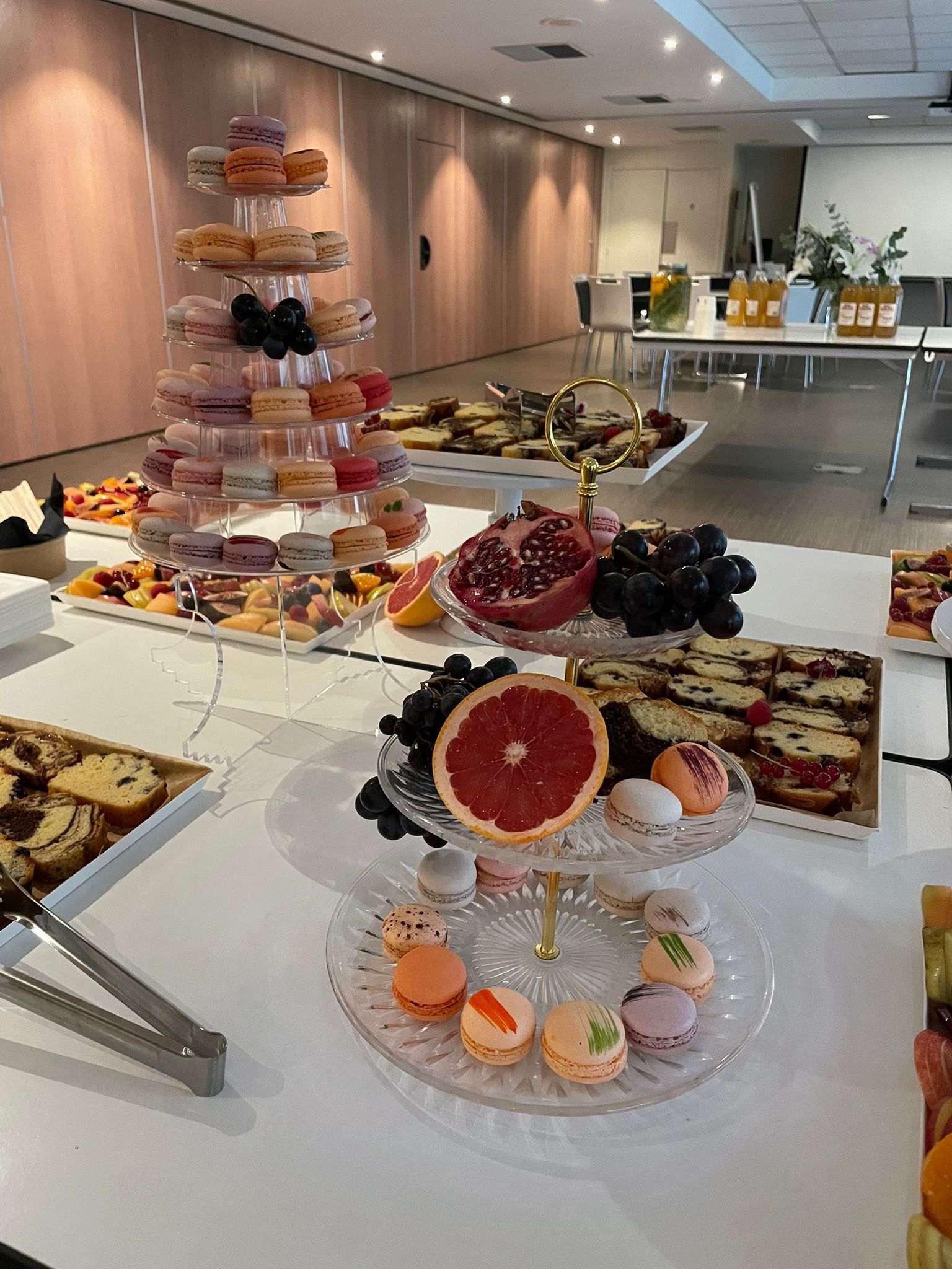 Buffet avec douceurs et fruits, dont tour de macarons, dans une salle lumineuse.