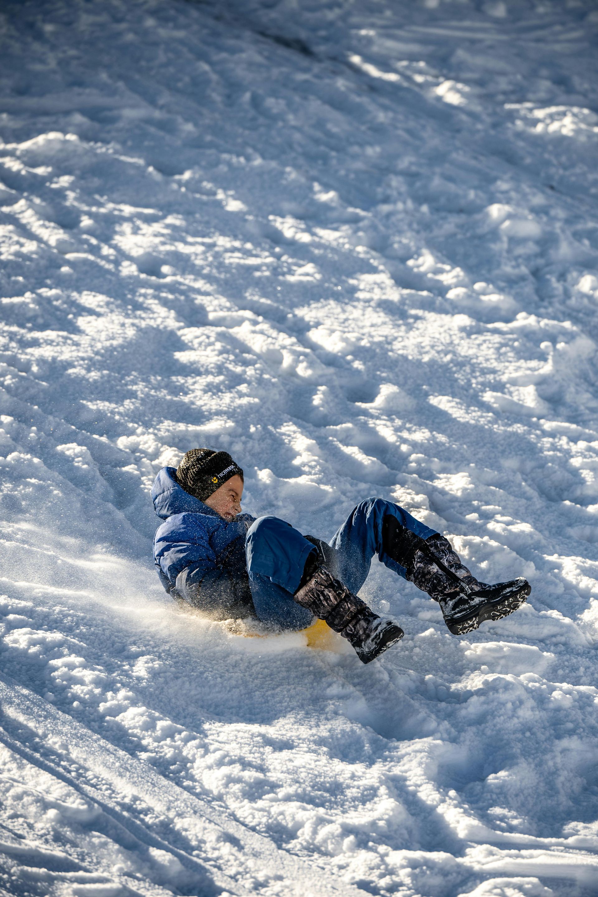 Un jeune garçon glisse sur une colline couverte de neige.