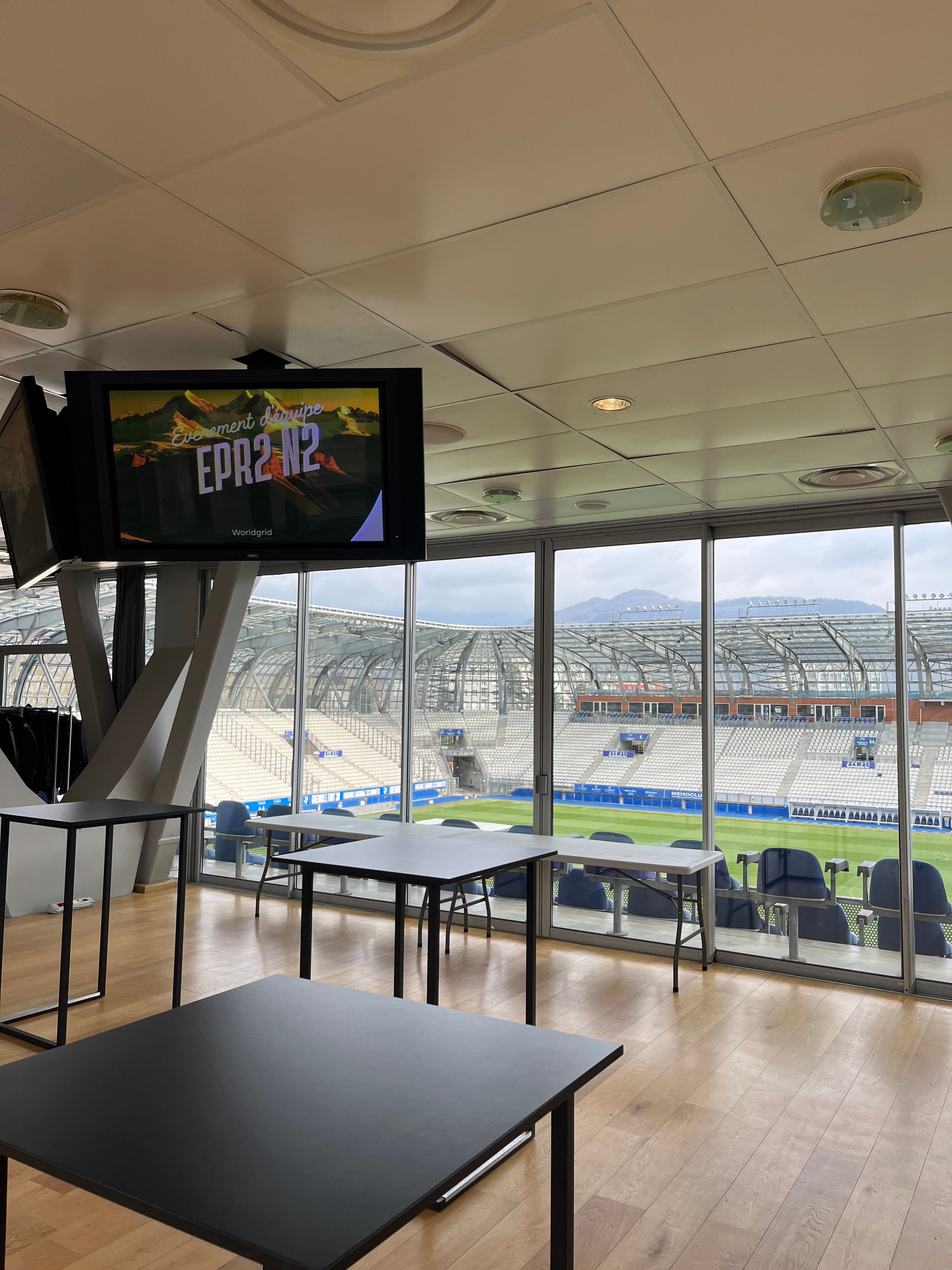 Une grande télévision est suspendue au plafond dans une pièce avec des tables et des chaises.