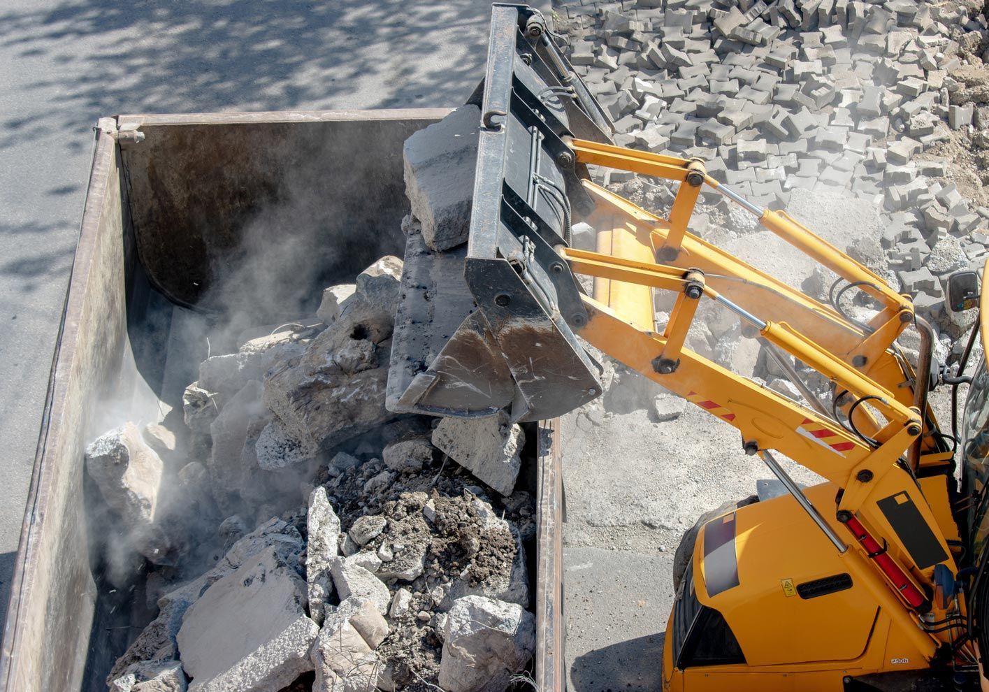 A yellow excavator is loading rocks into a dumpster