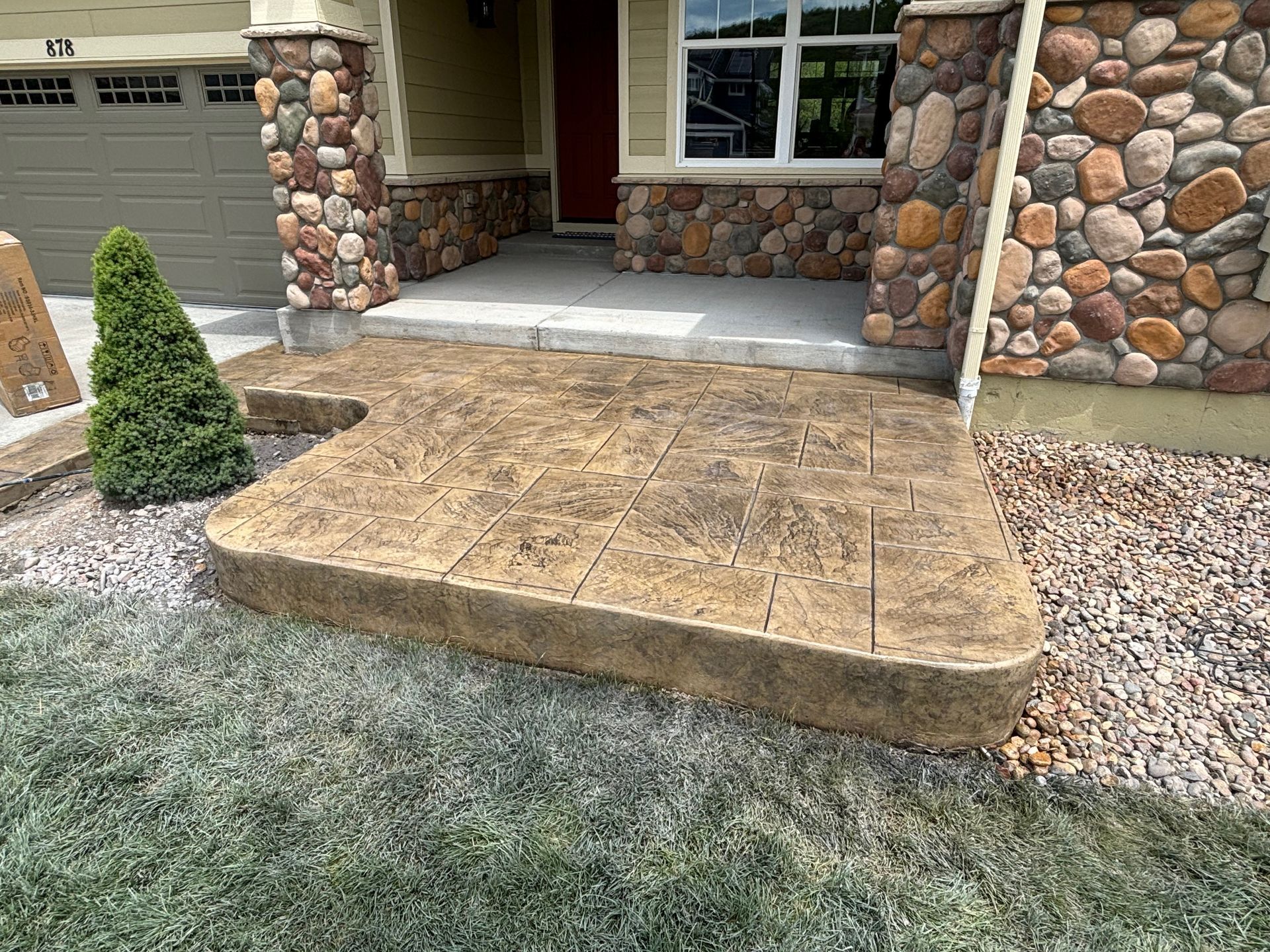 Front porch with stone facade and a small ramp leading to the entrance, bordered by gravel and a frosted lawn.