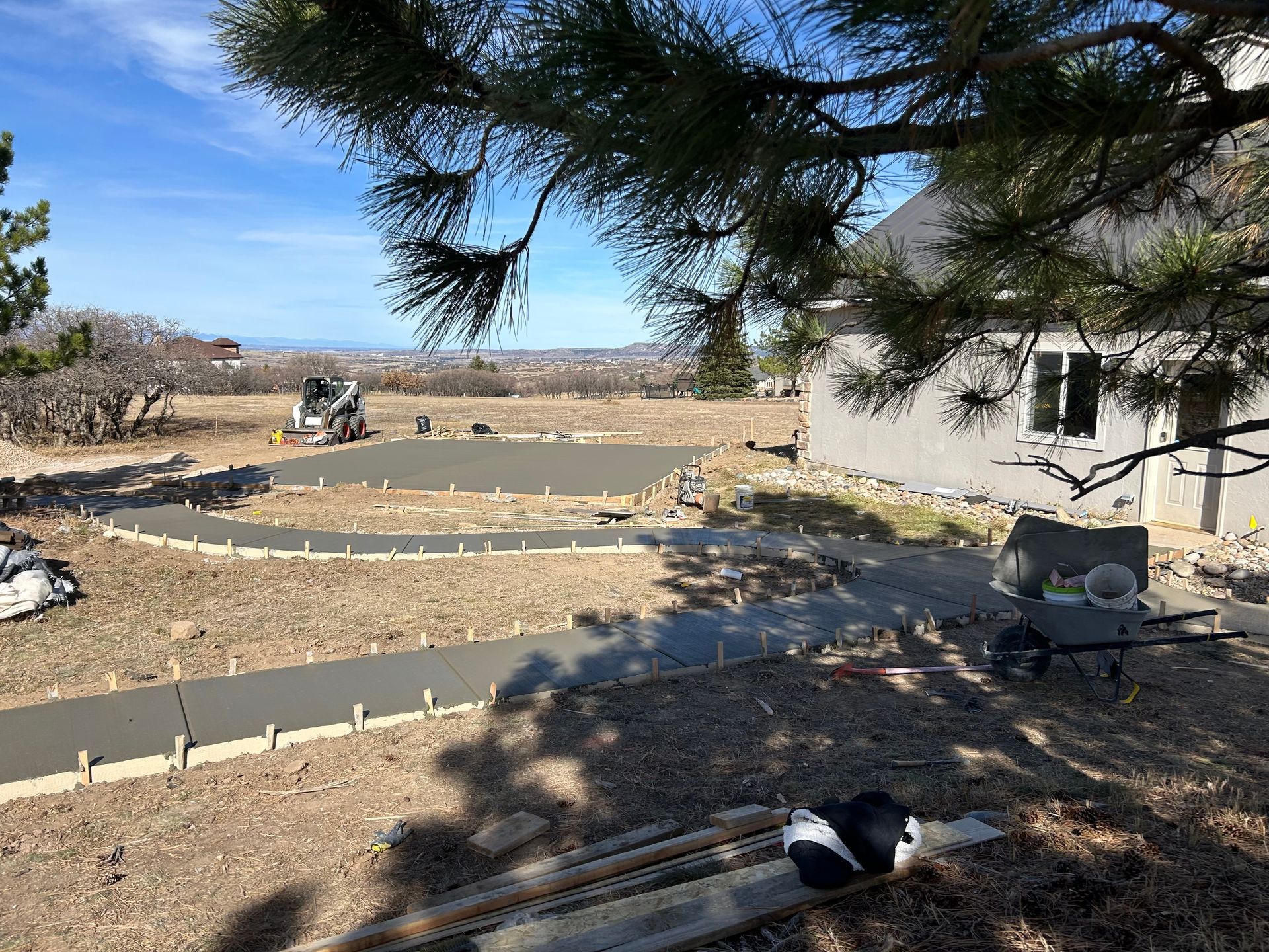 Desert garden construction with curved stone borders, a house, and a pine tree casting shade.