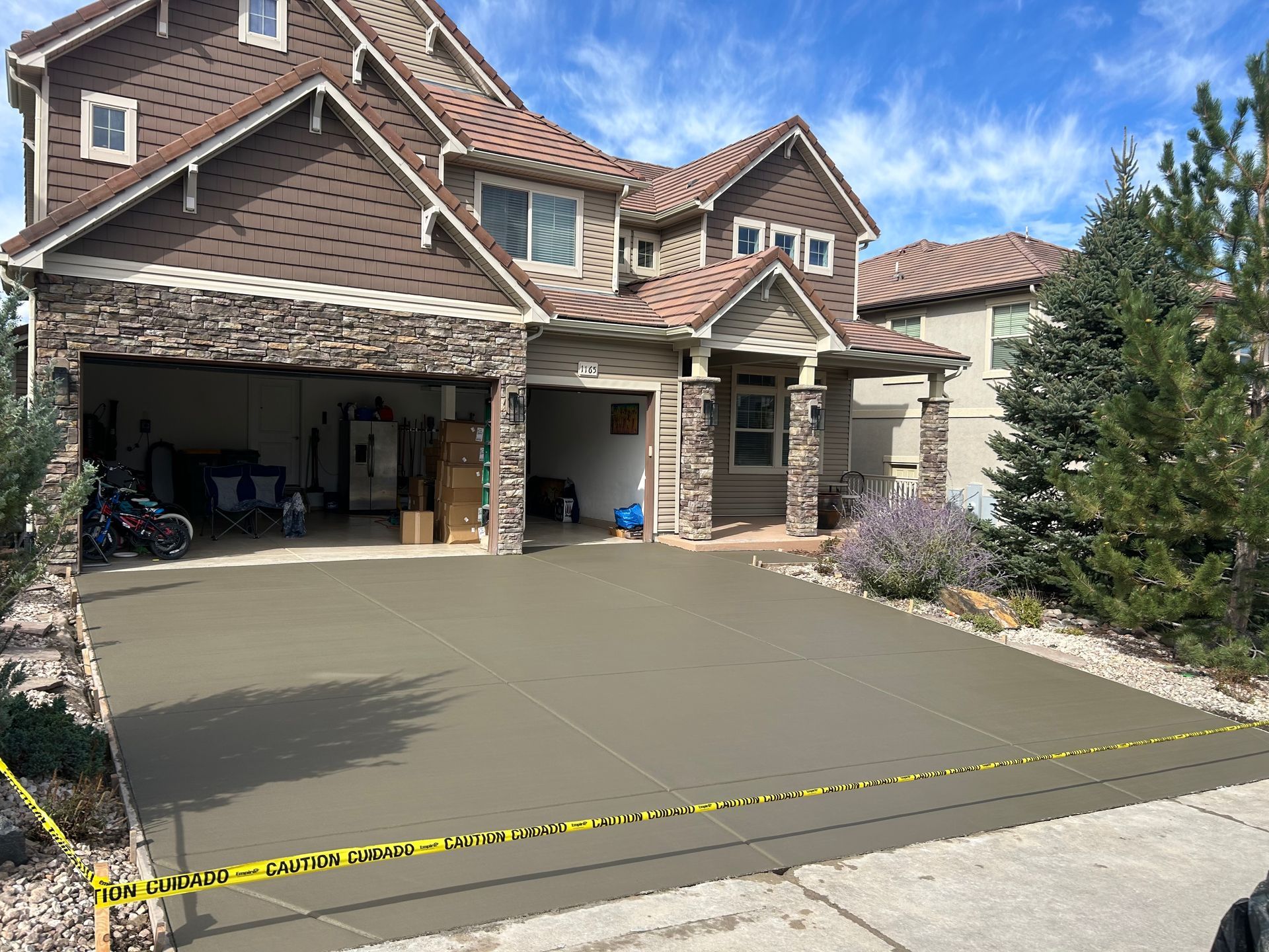 Front driveway of a brick house with a three-car garage, concrete apron, and yellow caution tape across the front.
