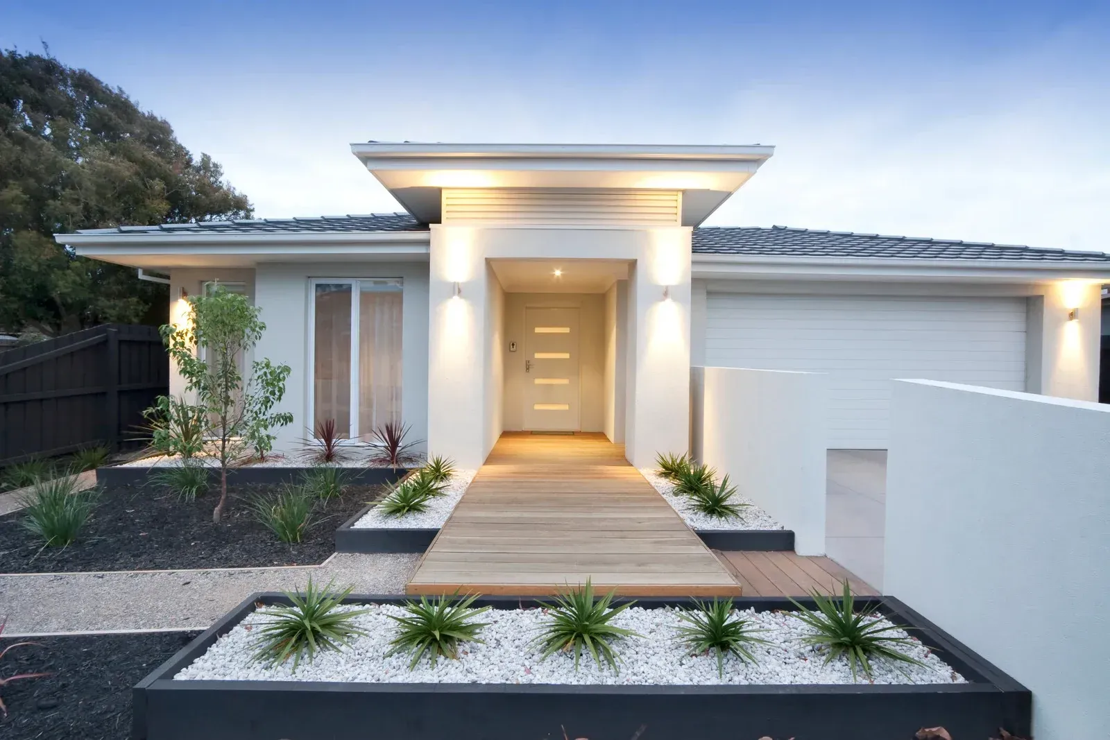 Modern home exterior with wooden walkway, landscaped front yard, and garage.