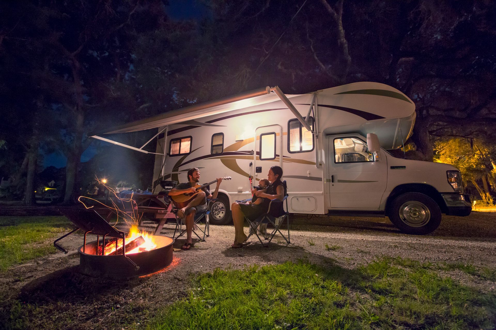 A couple is sitting around a campfire in front of a rv at night.  | Cecelia Cook & Assoc. | Greenwood SC