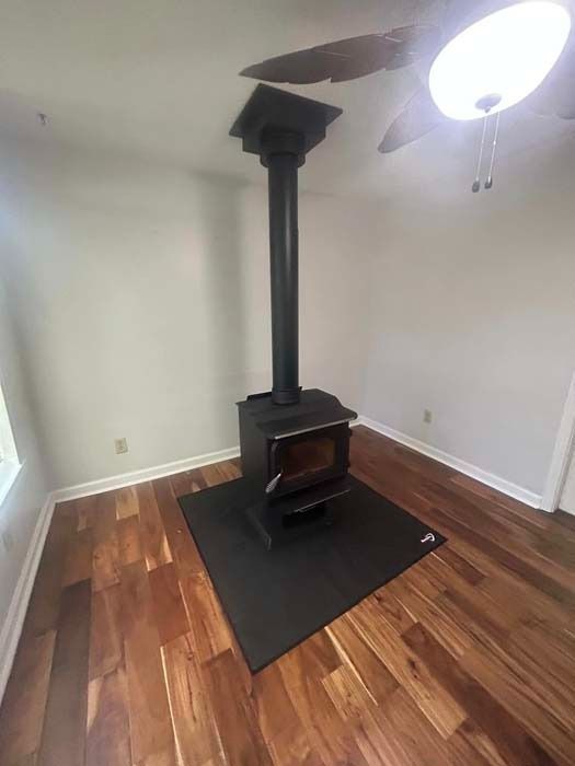 Wood-burning stove with black pipe in a room with hardwood floors.