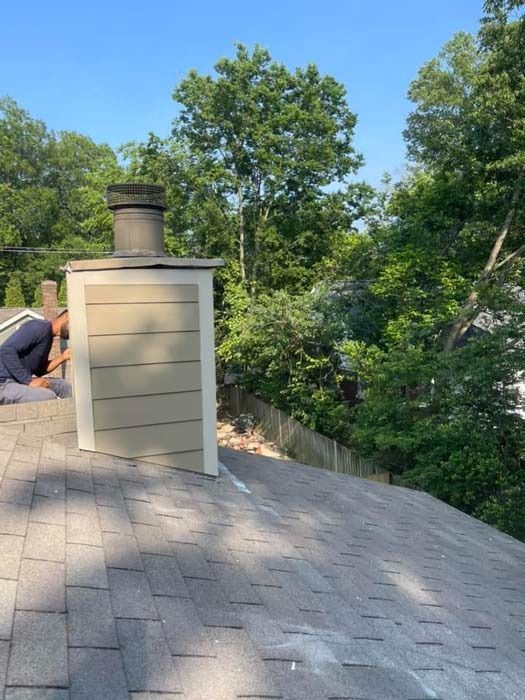 A person working on a chimney on a roof with green trees and blue sky in the background.