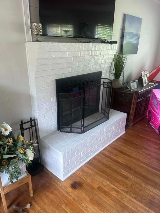 White-painted brick fireplace with a black screen and TV above, set in a room with hardwood floors.