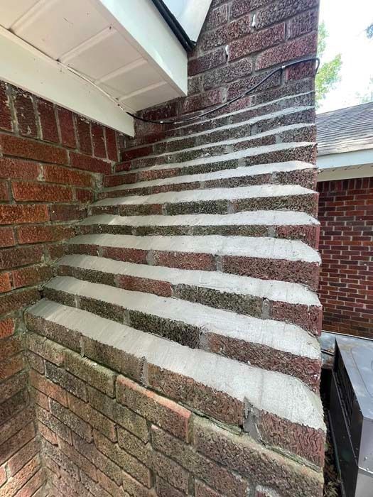 Brick chimney with angled, stepped top; white mortar; tan brick; against white soffit.