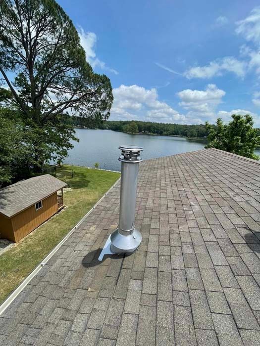 Chimney on a shingled roof overlooking a lake on a sunny day.