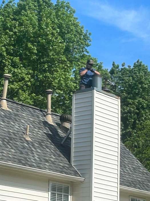 Man on chimney, inspecting. Blue sky, green trees in the background.