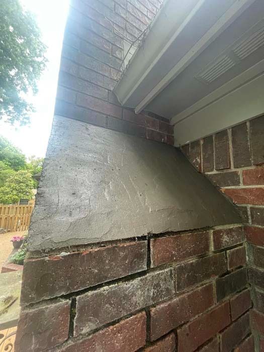 Brick chimney corner with gray concrete and white trim, outdoors.