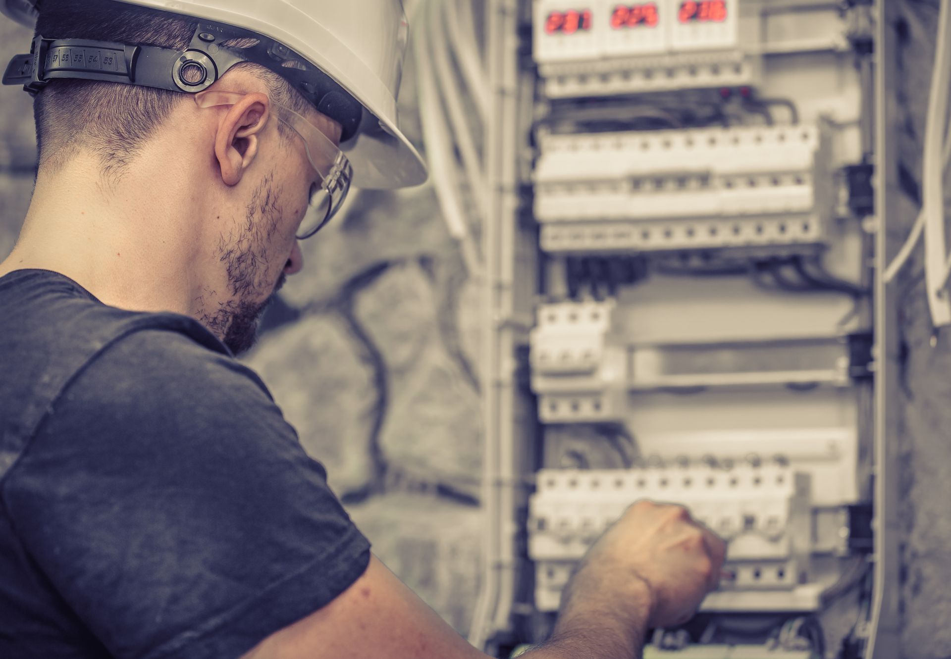 A male electrician works in a switchboard with an electrical connecting cable.