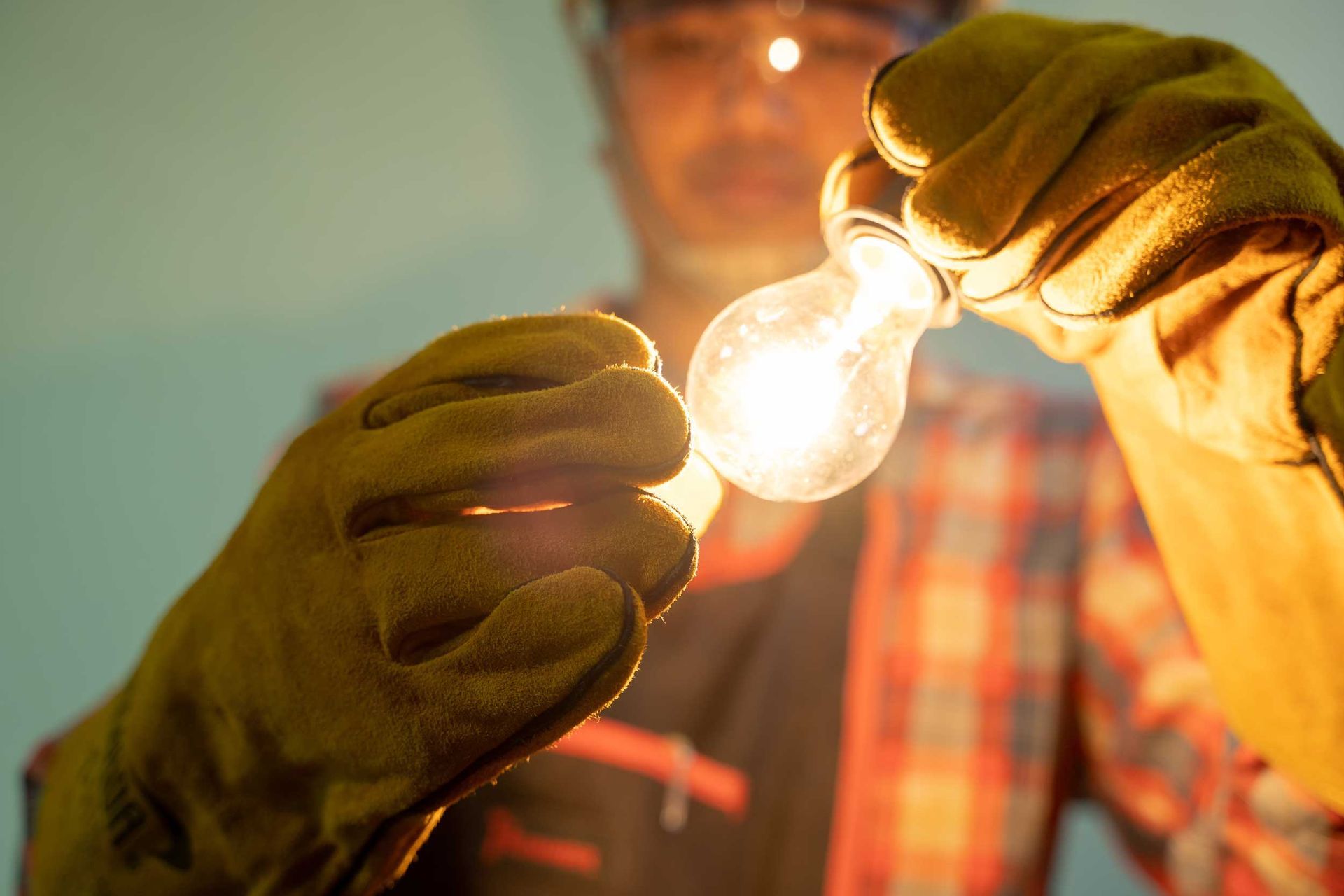 A male electrician uses and handles a lit lightbulb.