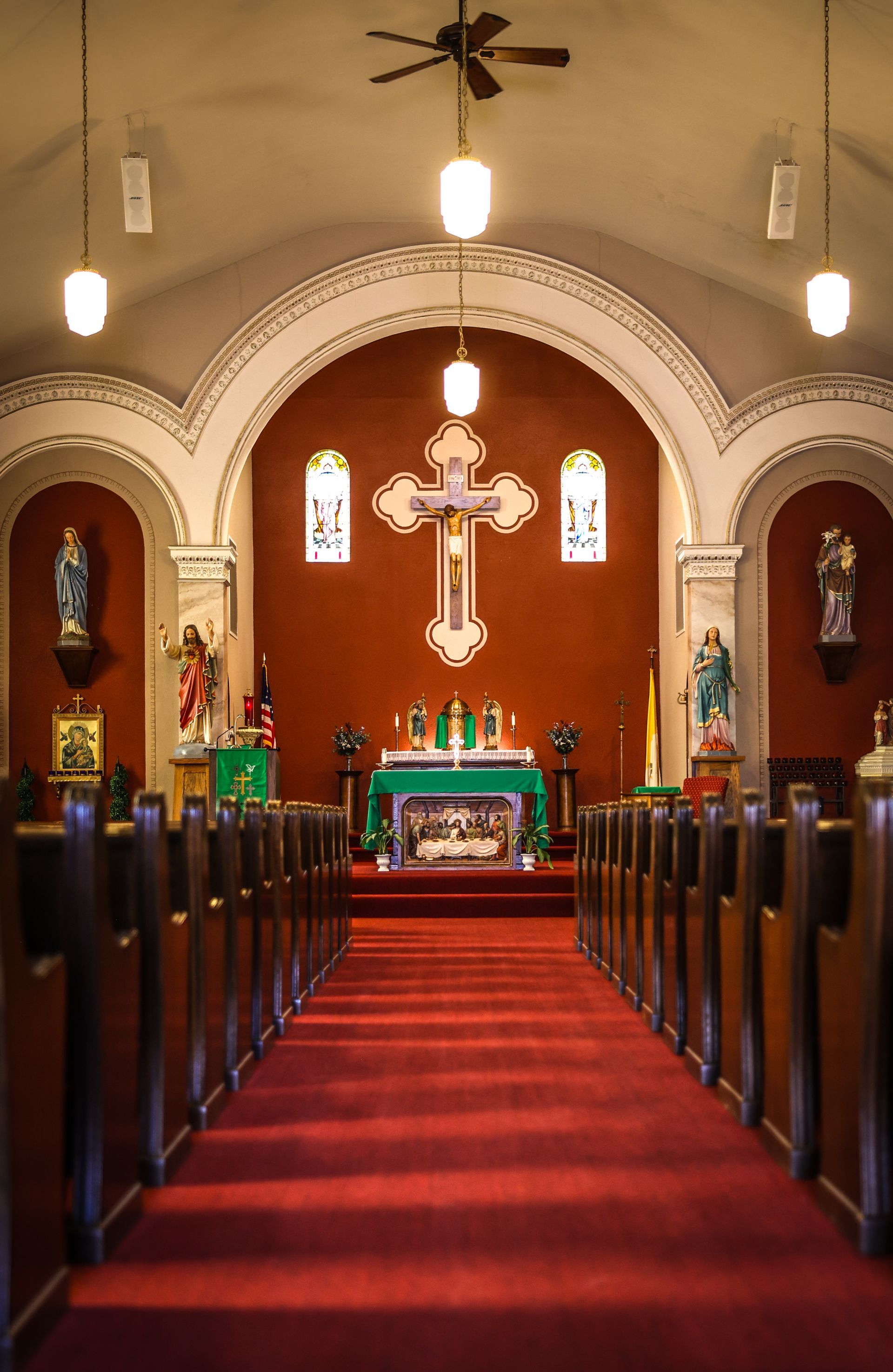 Interior of a St. Christina Catholic Church with a red carpet aisle leading to an altar and a large crucifix. Wooden pews line both sides.