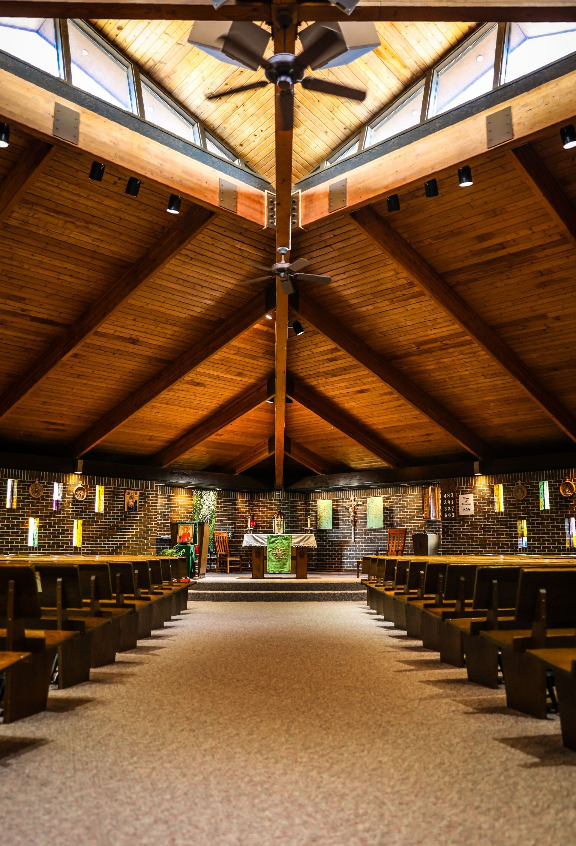 Interior view of St. Magdalen Catholic Church with a wooden, high-ceilinged and rows of pews, a central altar, and a skylight. Warm wood tones dominate.