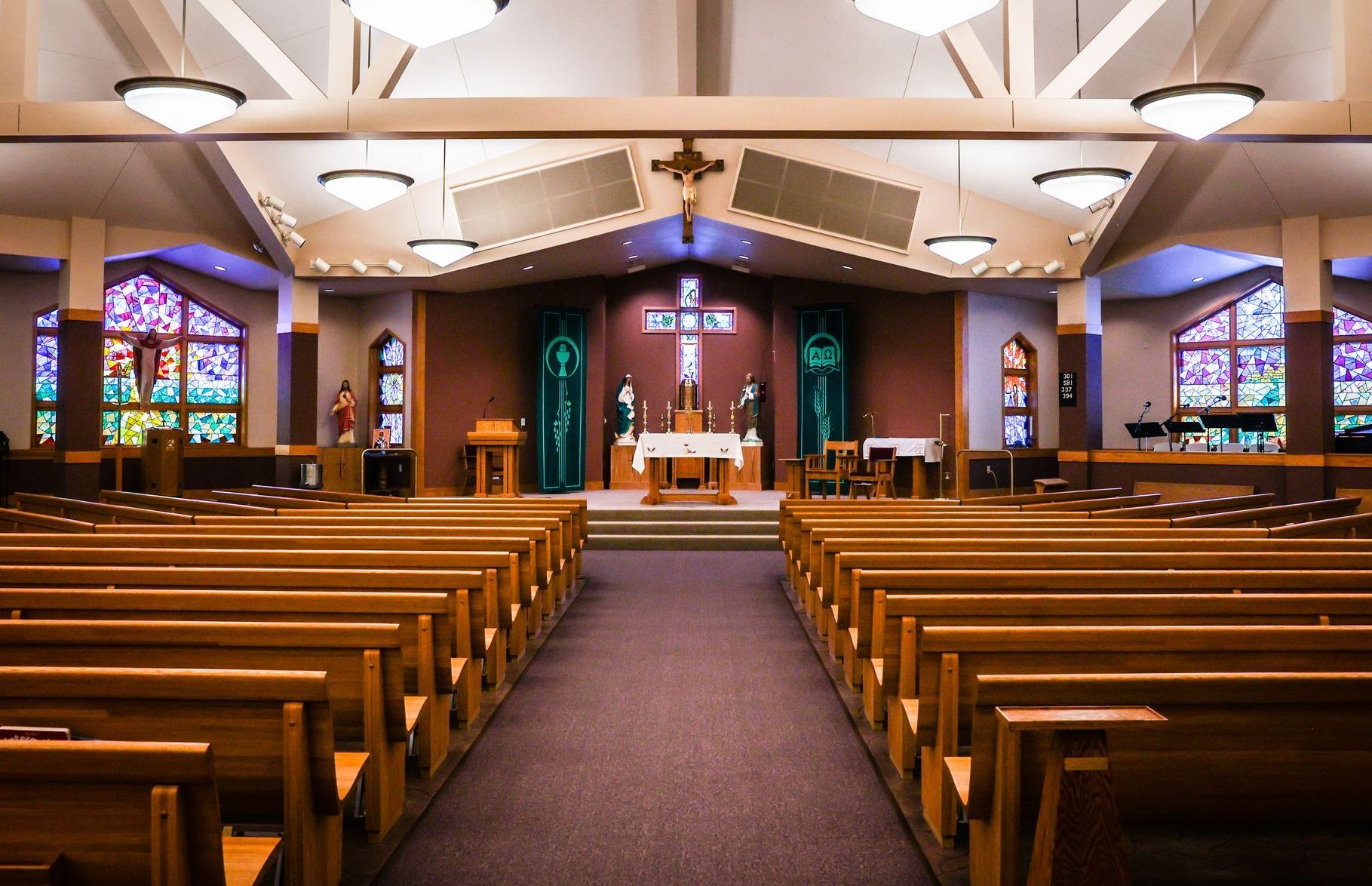 Interior view of a St. Nicholas Catholic Church sanctuary with rows of wooden pews facing the altar, stained glass windows, and a cross.