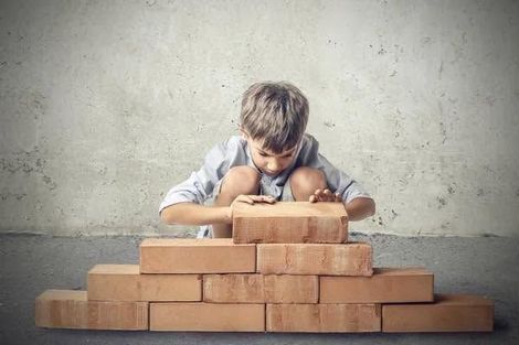 This is a photograph of a little boy building a wall with cement blocks.