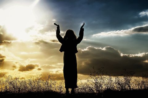 This is a beautiful image of a silhouette of a woman with her arms raised in prayer.