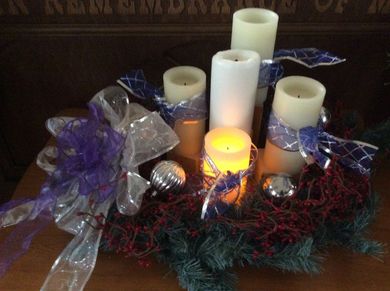 This is a photograph of an advent wreath with one candle burning.