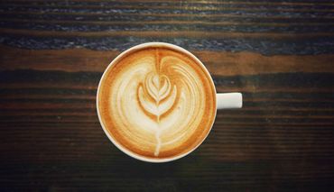 This is a photograph of a coffee cup filled with coffee and a flower is imprinted in the foam on the top.