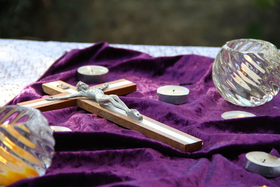 This is an image of a cross and candles sitting on a piece of purple cloth.