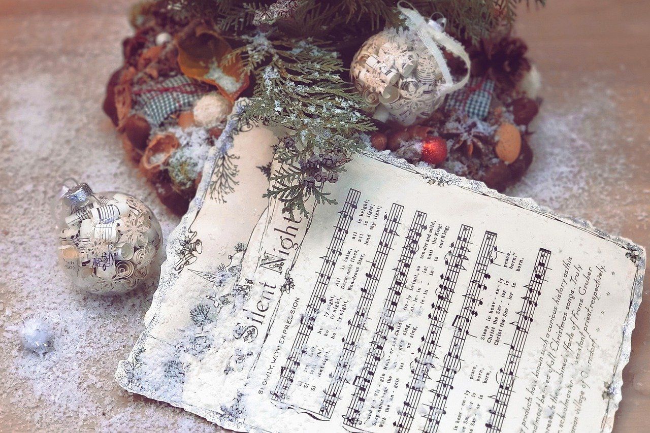 This is an image of an open book of music with an evergreen branch and Christmas bells resting on it.