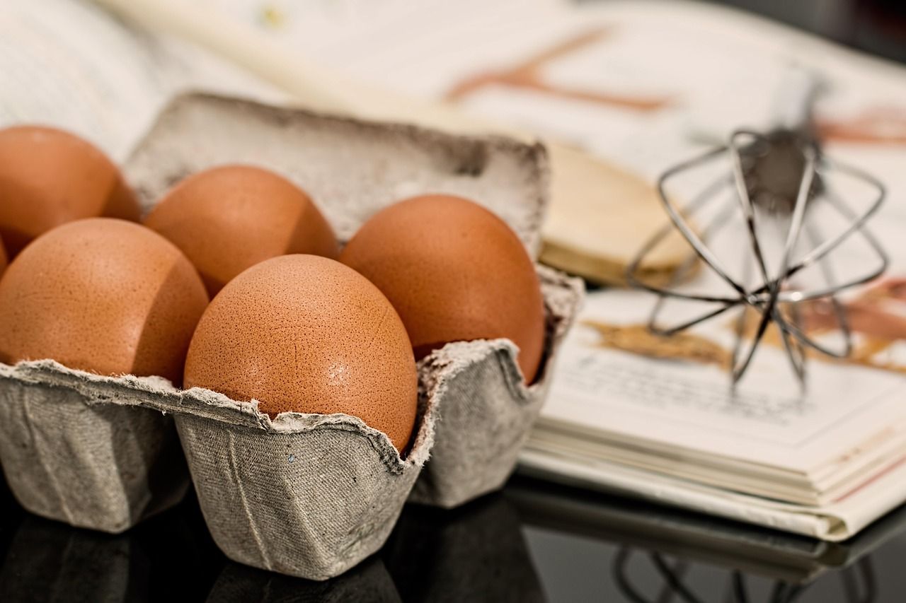 This is a photograph of a recipe book, a whisk and eggs.