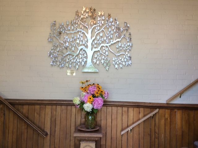 Thus is a photograph of a metal sculpture of a tree with flowers in front of it.