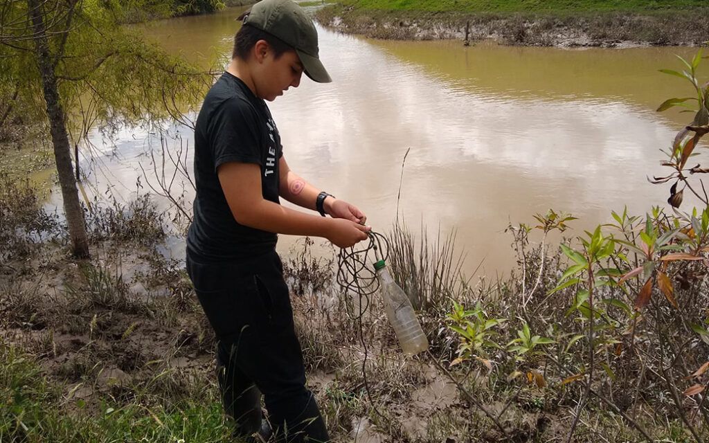 Un niño pequeño está parado en el barro cerca de un cuerpo de agua.