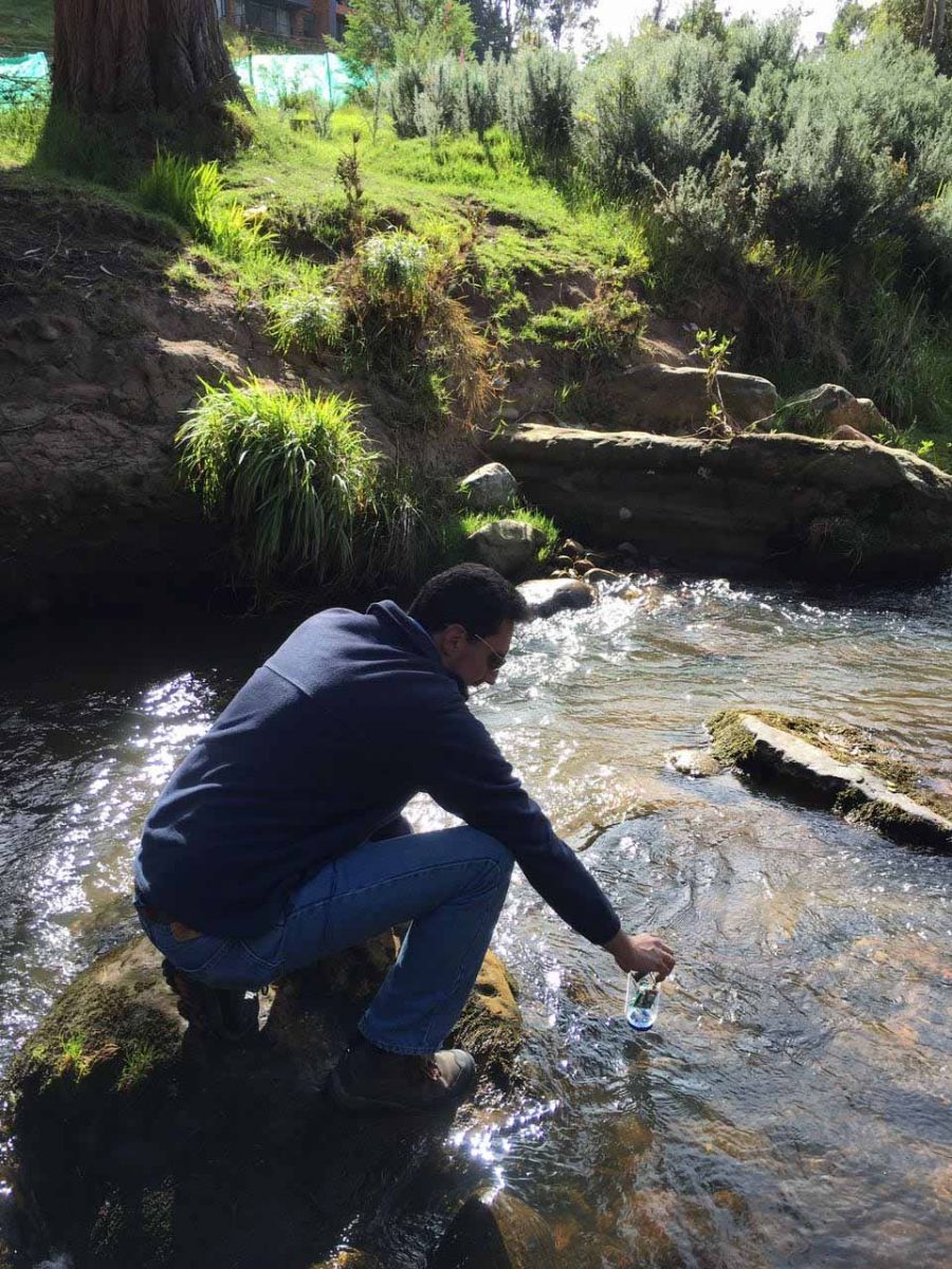 Un hombre está arrodillado en un arroyo sosteniendo una botella de agua.