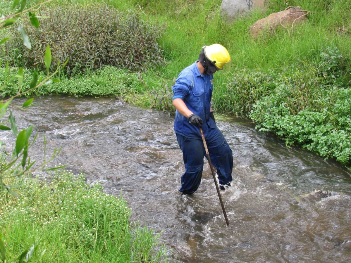 Un hombre que lleva un casco está parado en un río sosteniendo un palo.