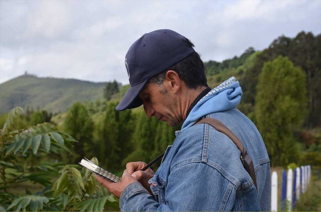 Un hombre que lleva una gorra de béisbol y una chaqueta vaquera está escribiendo en un trozo de papel.