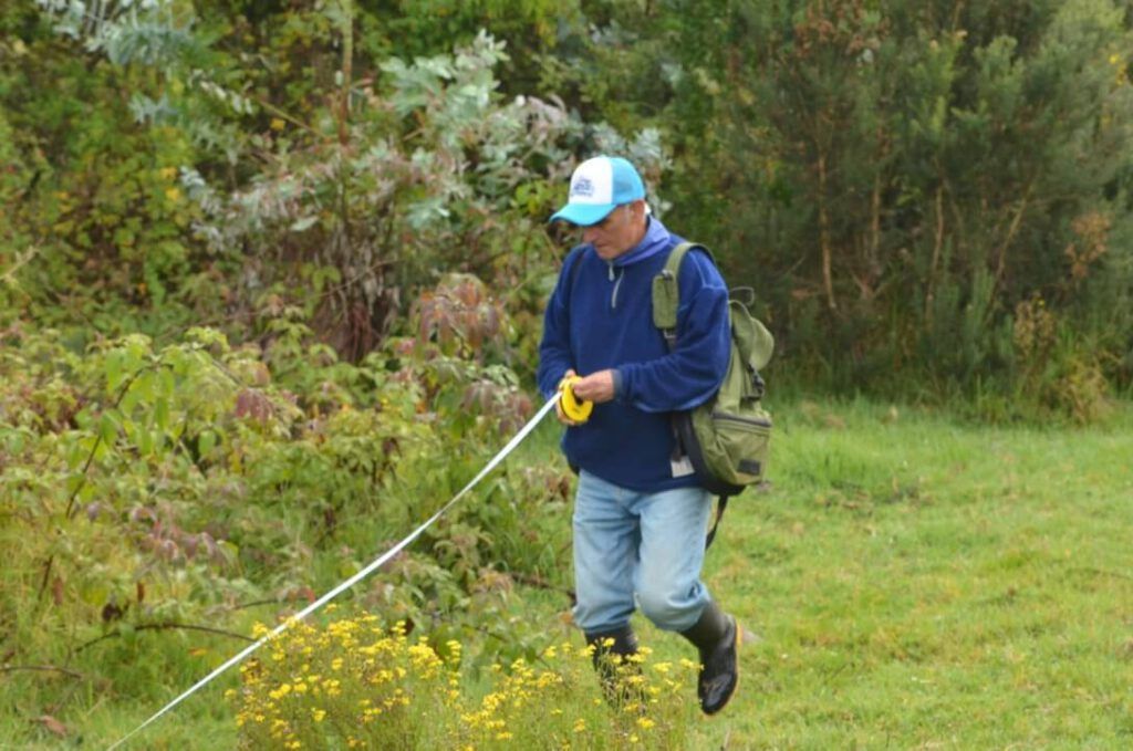 Un hombre está parado en un campo sosteniendo una cinta métrica.